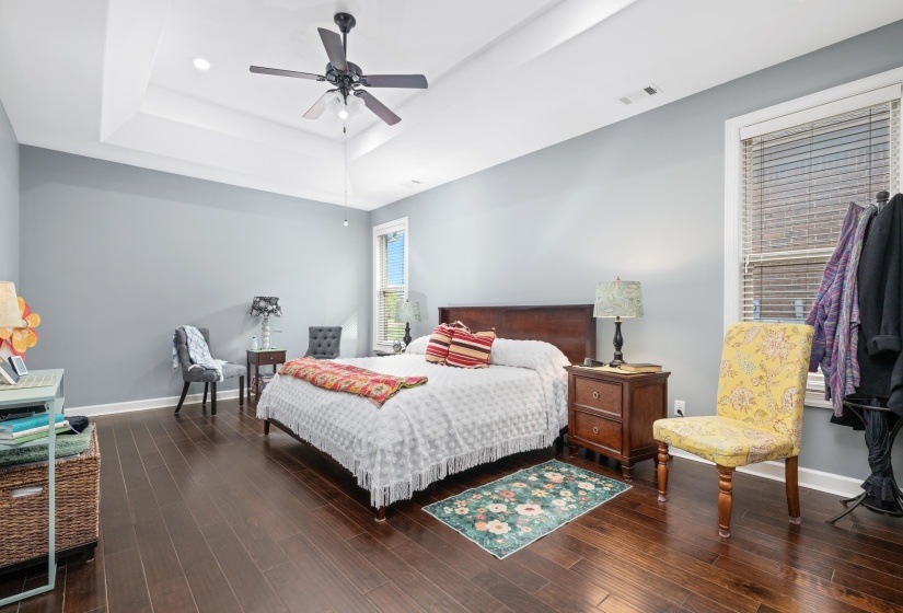 Spacious bedroom featuring dark wood-finish flooring, a tray ceiling with a ceiling fan, and recessed lighting