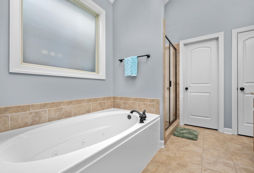 Soaking tub with bronze fixtures, ceramic tile flooring, and a glass-enclosed shower