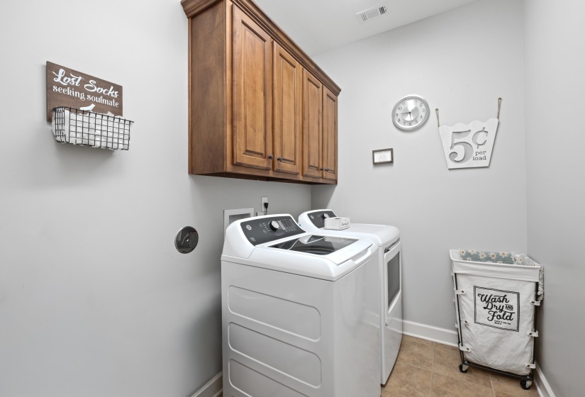 Dedicated laundry room featuring built-in wood cabinetry, light neutral wall paint, tile flooring, and white baseboards