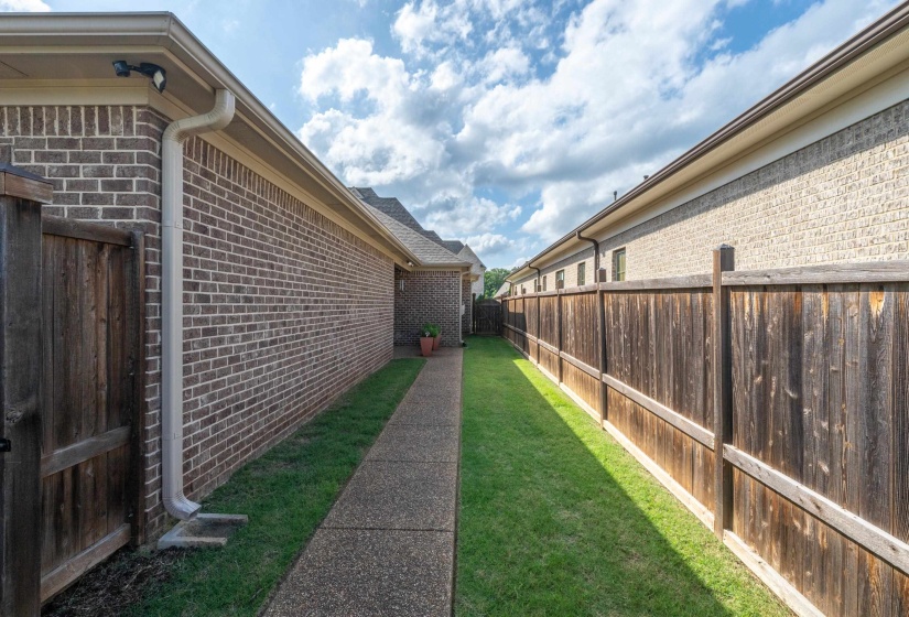 Side yard with a concrete walkway, green lawn, and privacy fencing