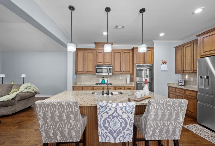 Kitchen featuring a large island with sink, pendant lighting, stainless steel appliances, wood-finish cabinetry, and crown molding