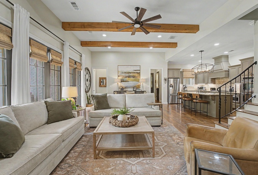 Spacious living area featuring exposed wood ceiling beams, wood-finish flooring, and a ceiling fan