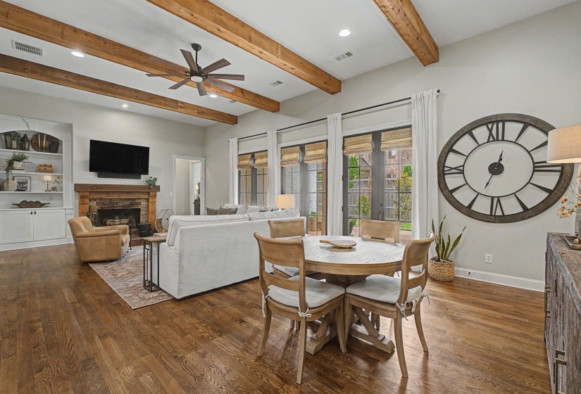Spacious living area featuring wood-finish flooring, exposed ceiling beams, and a stone fireplace with a wood mantle