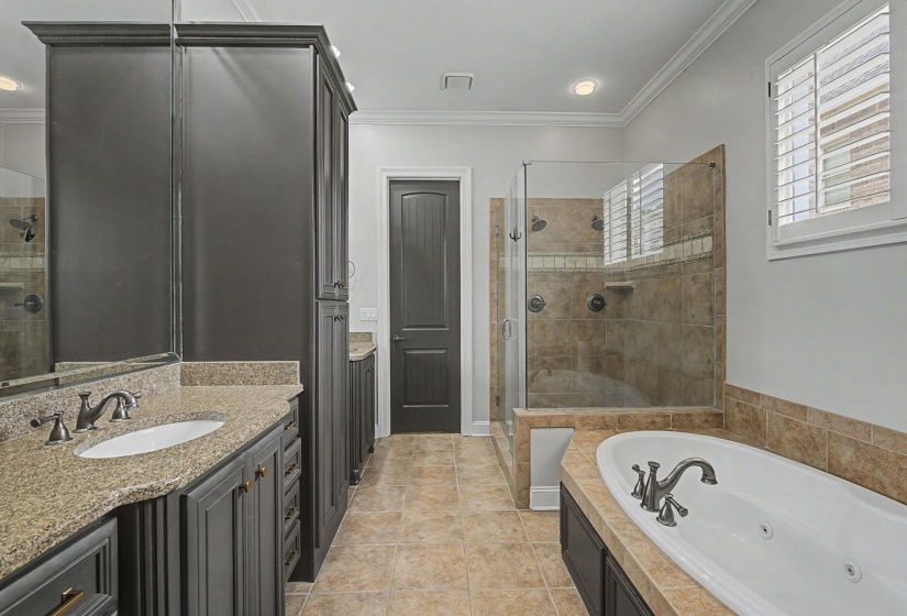 Bathroom featuring a dual vanity with granite countertops, a built-in soaking tub, and a separate glass-enclosed shower with tile surround