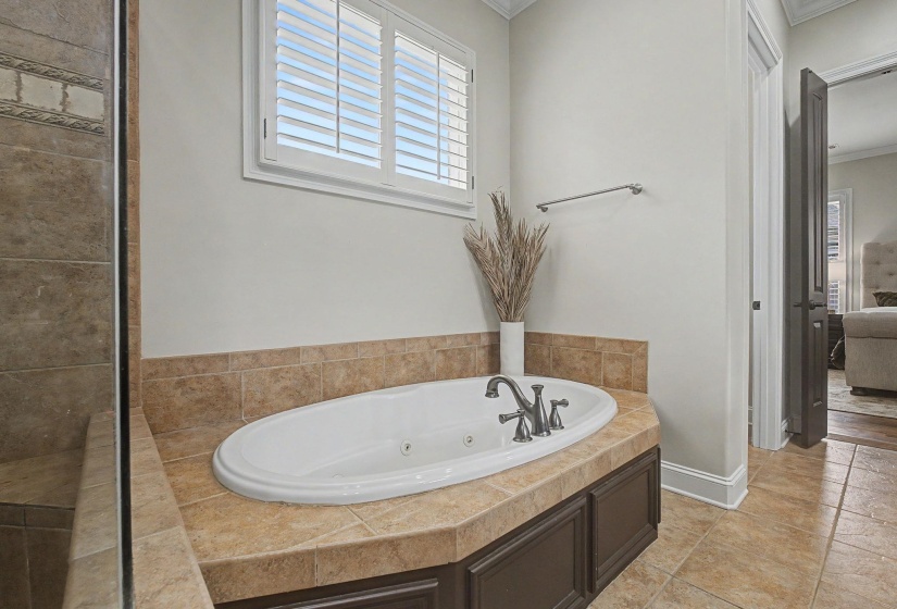 Built-in soaking tub with tile surround, white plantation shutters, tile flooring, and dark wood-finish cabinet base