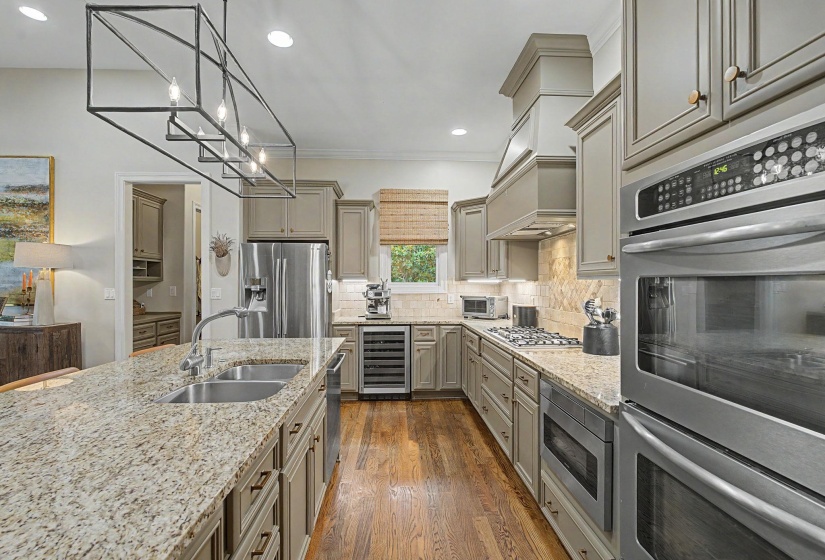 Gourmet kitchen featuring granite countertops, stainless steel appliances including double ovens and a gas range, custom cabinetry, and wood flooring