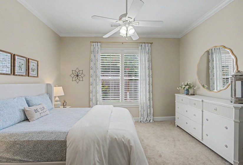 Carpeted room featuring crown molding, a window with plantation shutters, a ceiling fan with integrated lighting, and a broad dresser