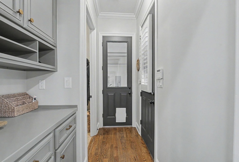 Hallway featuring wood-finish flooring, two gray doors, and a built-in cabinetry system with open shelving and gold-tone hardware