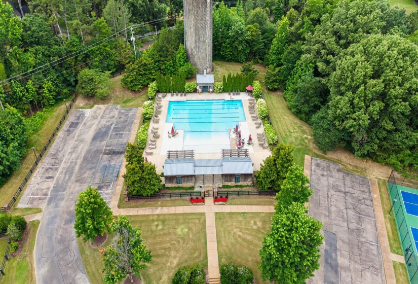 Community swimming pool with surrounding lounge chairs and red umbrellas, alongside a clubhouse with metal roofing