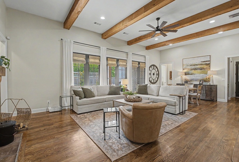 Spacious living area featuring exposed wood ceiling beams, a ceiling fan with light, recessed lighting, and rich wood-finish flooring