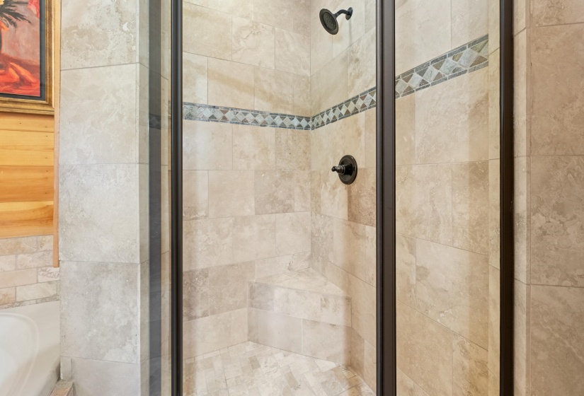 Glass-enclosed shower featuring natural-tone tile, decorative accent tile band, built-in shower bench, and a dark bronze showerhead and control