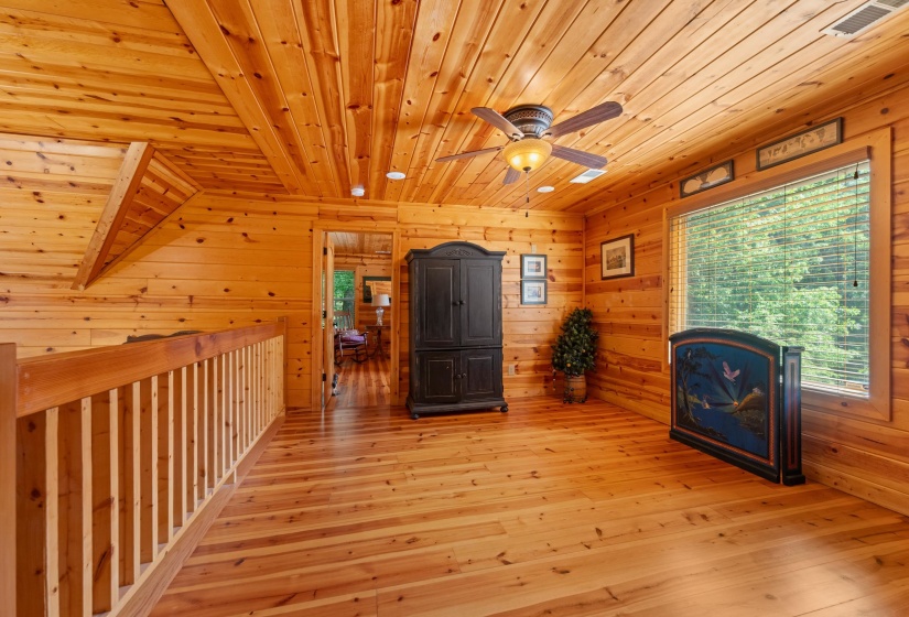 Warm wood-paneled room featuring a ceiling fan with integrated lighting, wood-finish flooring, and a large window with horizontal blinds