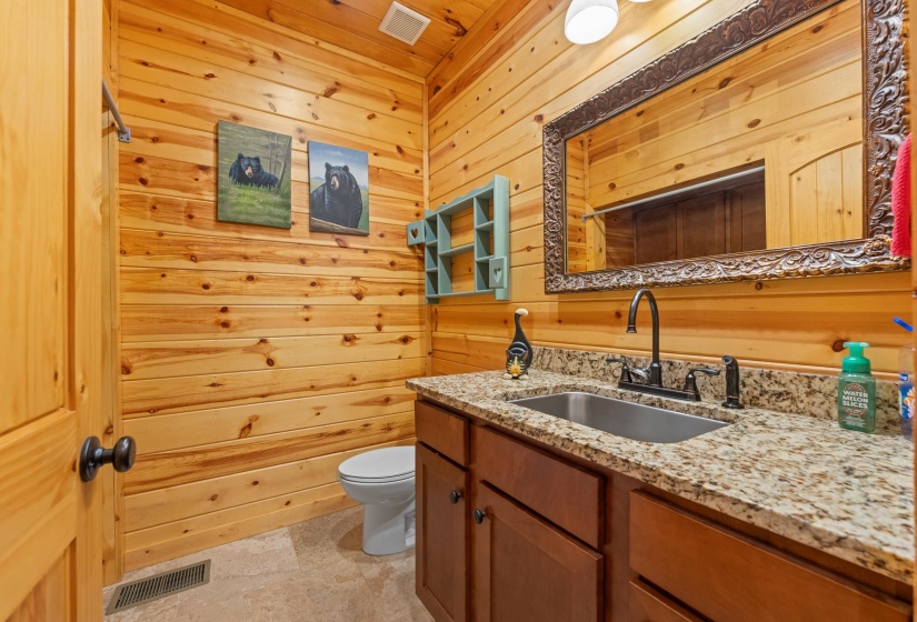 Bathroom featuring natural wood plank walls, a dark wood vanity with a light granite countertop, an undermount sink, and an ornate framed mirror