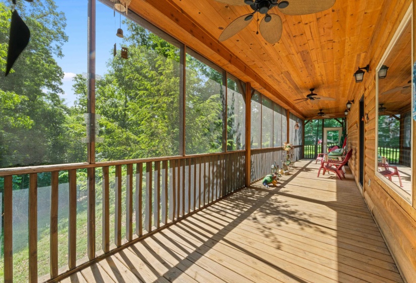 Expansive screened porch featuring wood-finish flooring, a natural wood paneled ceiling, multiple ceiling fans, recessed wall sconces, and a verdant tree line backdrop
