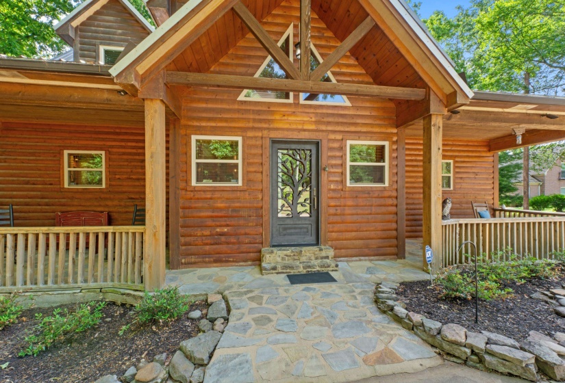 Log cabin exterior featuring a covered front porch, decorative front entry door, stone walkway, and natural wood railings