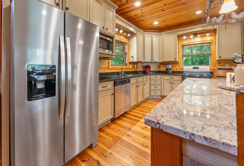 Kitchen featuring wood-finish flooring, light-toned cabinetry, stainless steel appliances, granite countertops, and wood paneling on walls and ceiling