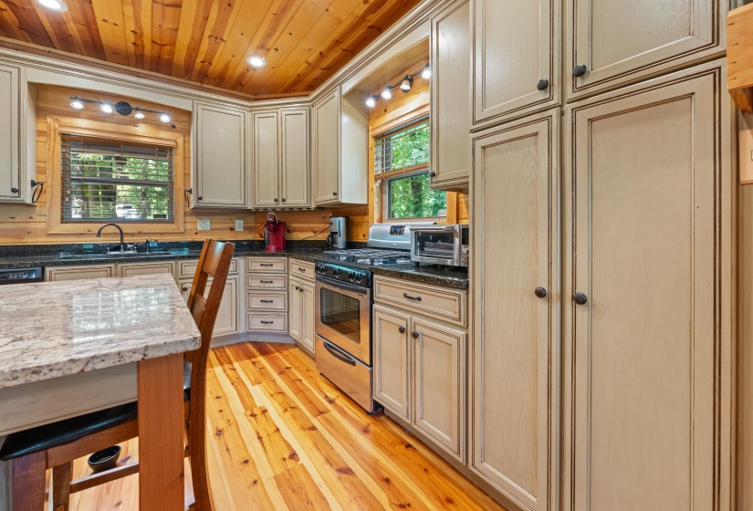 Kitchen featuring wood-finish flooring, a wood-paneled ceiling, light-toned cabinetry, dark countertops, and stainless steel appliances