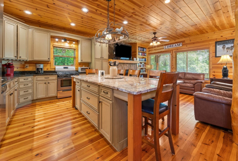 Expansive open-concept living space featuring wood-paneled walls and ceilings, wood-finish flooring, a kitchen island with stone countertop, stainless steel range, and built-in shelving