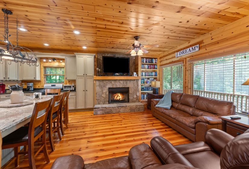 Open-concept living space featuring wood-finish flooring, a stone fireplace, and extensive wood paneling