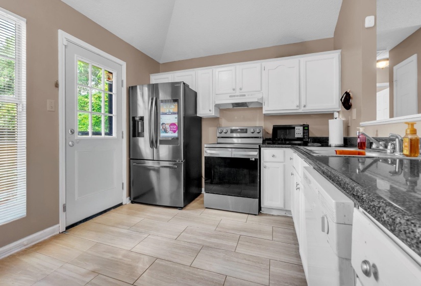 Kitchen featuring stainless steel appliances, wood-finish tile flooring, white cabinetry, dark speckled countertops, and a full-light exterior door