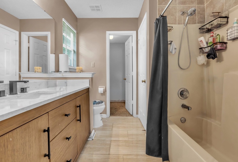 Bathroom featuring a wood-finish vanity with a light-toned countertop, matte black hardware, and a framed mirror