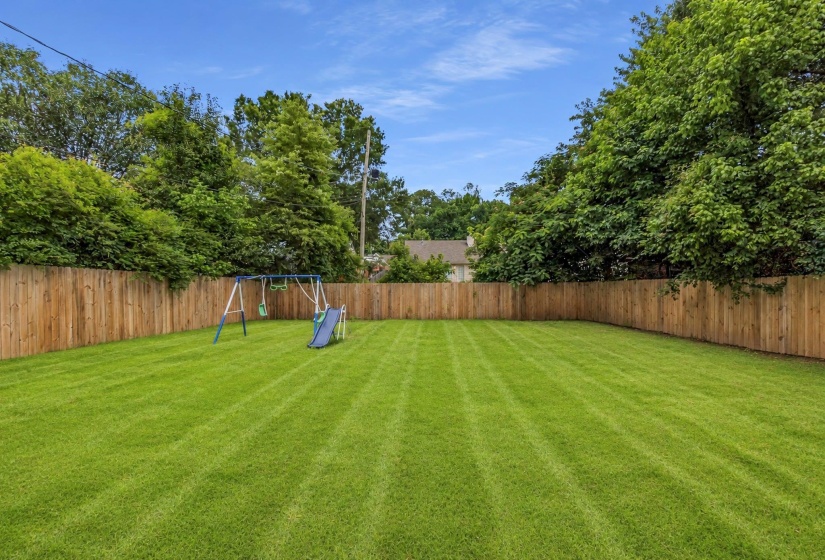 Expansive lawn with a wooden privacy fence and mature perimeter trees