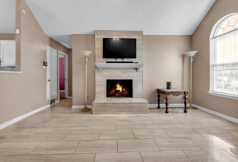 Living area featuring a tile fireplace with a mantel, a large arched window with interior blinds, and light-toned tile flooring