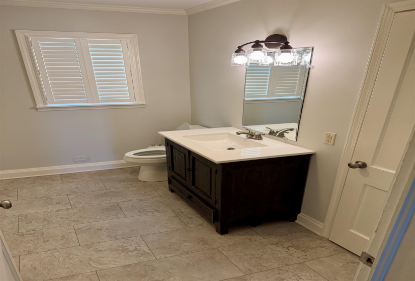 Bathroom featuring a dark wood vanity with an integrated sink, a contemporary three-light fixture, and a framed mirror