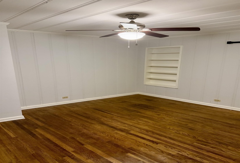 Spacious room featuring rich wood-finish flooring, white paneling, and a built-in shelving unit