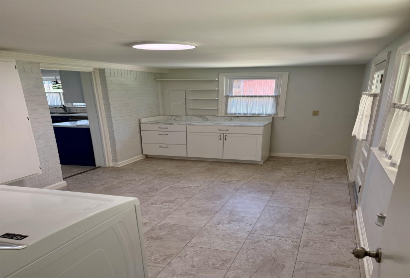 Utility room featuring light-colored tile flooring, white cabinetry with silver hardware, and a window with white trim
