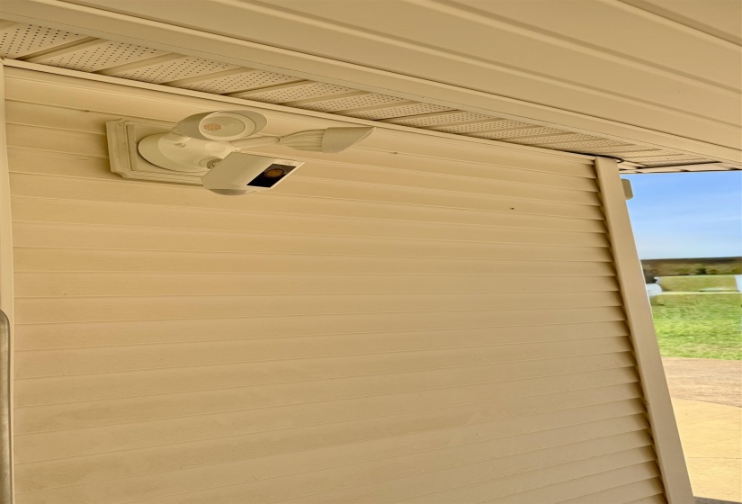 Exterior light fixture with integrated camera, mounted on tan horizontal siding