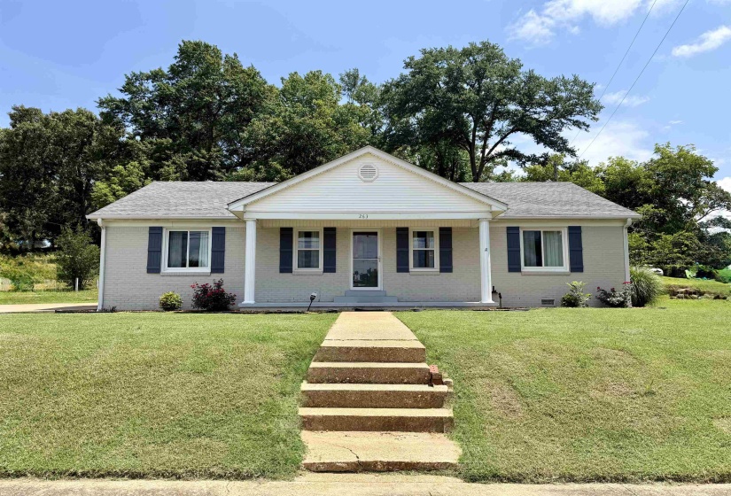 Ranch-style residence featuring a light-colored brick exterior, dark blue window shutters, and a covered porch entry