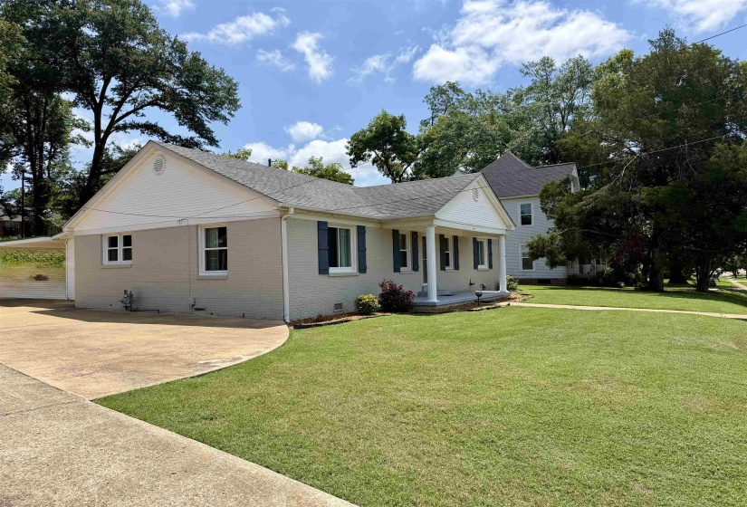 Traditional single-story residence featuring a covered front porch with white columns, light-colored brick exterior, and dark shutters