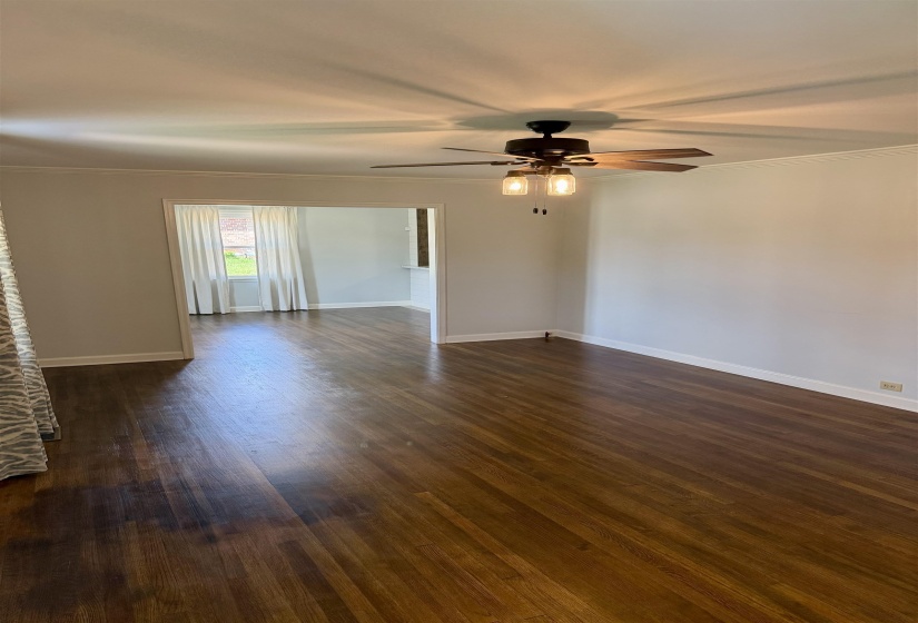 Spacious room featuring wood-finish flooring, light-toned walls, and a ceiling fan with integrated lighting
