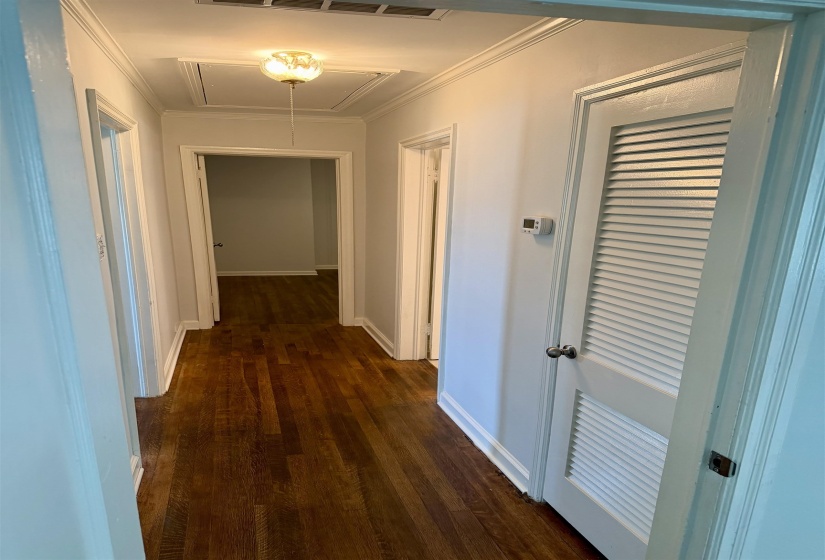 Hallway featuring wood-finish flooring, white baseboards, and crown molding