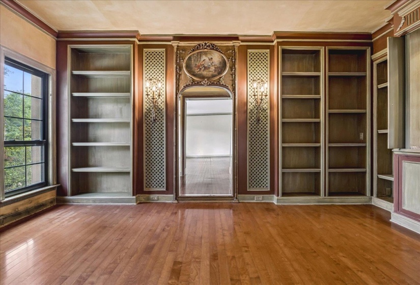 Hardwood flooring throughout featuring extensive built-in shelving, decorative wall sconces, and an arched doorway