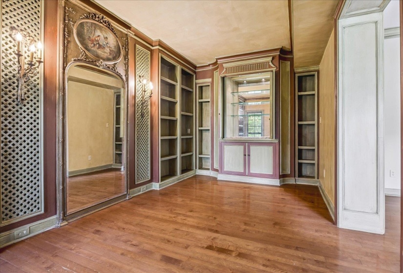 Interior space featuring wood-finish flooring, extensive built-in shelving, ornate wall sconces, and an integrated mirrored bar cabinet with glass shelving