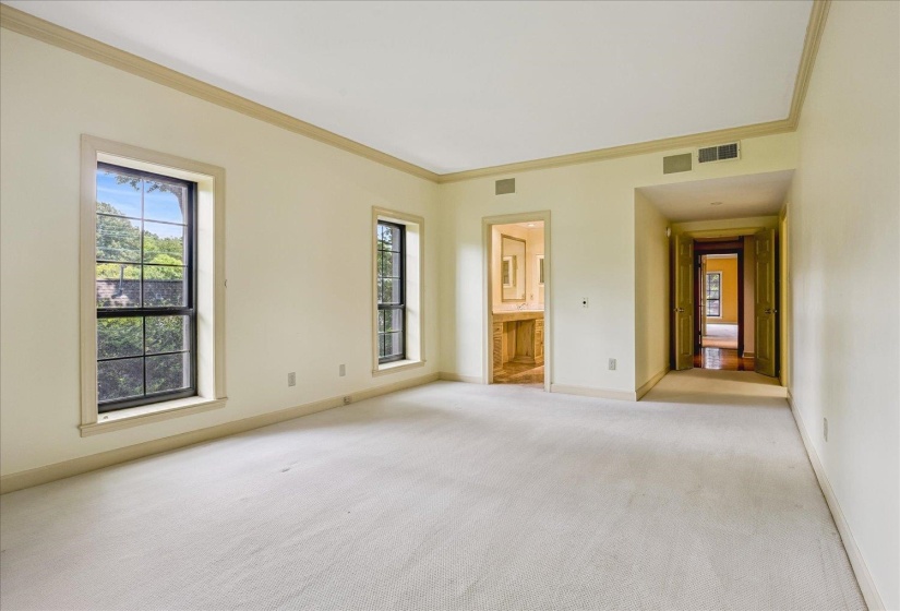 Spacious room featuring light-toned carpeting and multiple windows with exterior tree views