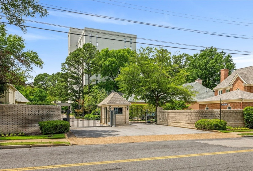 Gated community entrance with a brick perimeter wall, wrought iron gates, and a guardhouse