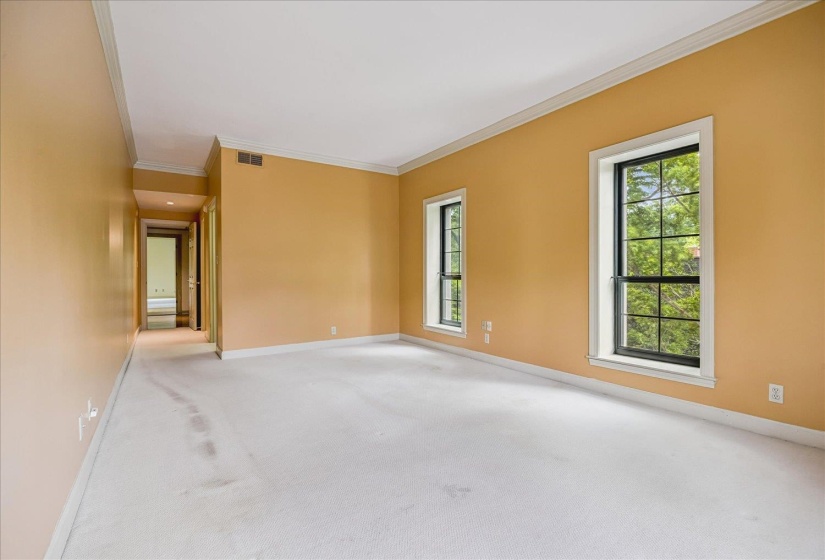 Spacious room featuring two large windows with black grilles, crown molding, and a hallway entry