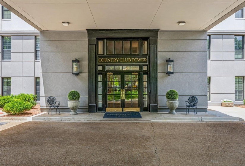 Building entrance featuring a prominent covered portico, double glass doors with dark framing, and exterior wall sconces