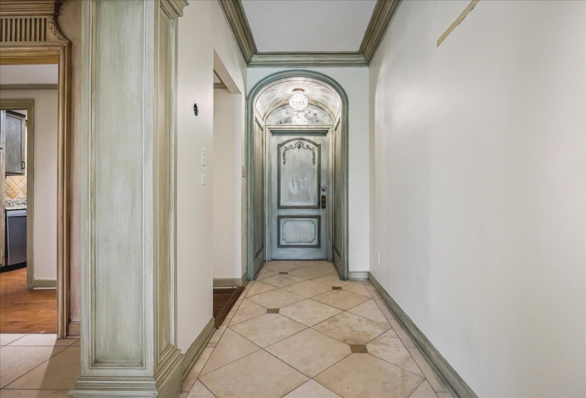 Hallway featuring ornate arched doorway with custom door, decorative ceiling light fixture, tile flooring with diamond accents, and extensive trim work