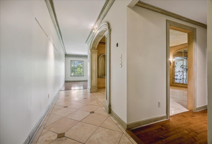 Hallway featuring patterned tile flooring, decorative arched doorway, crown molding, and contrasting baseboards
