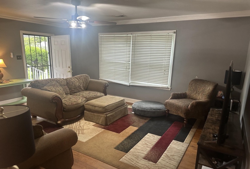 Living area featuring wood-finish flooring, a ceiling fan with integrated lighting, and crown molding