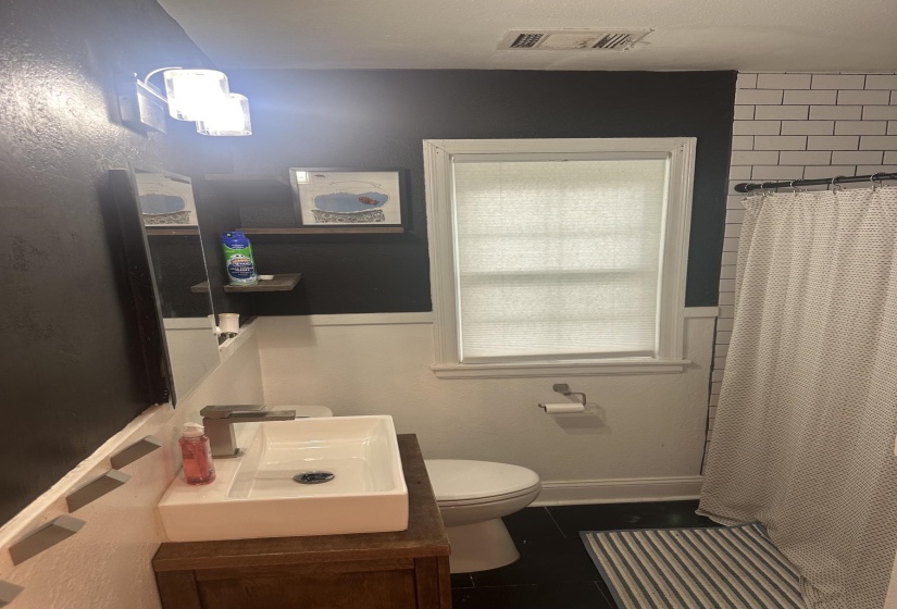 Bathroom featuring a vessel sink with a single-handle faucet, a window with a cellular shade, and subway tile shower surround