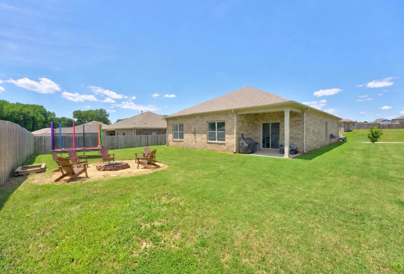 Expansive backyard featuring a dedicated fire pit area, a spacious covered patio, a wood privacy fence, and a brick exterior with multiple windows and sliding glass doors