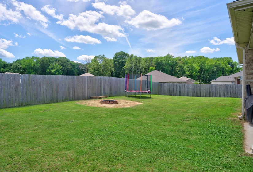Spacious backyard featuring a full privacy fence, mature perimeter trees, and a built-in fire pit
