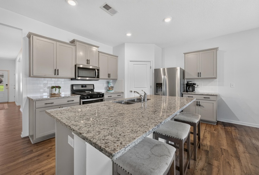 Kitchen featuring a large island with a double sink, light-toned cabinetry, stainless steel appliances, a white subway tile backsplash, and wood-finish flooring