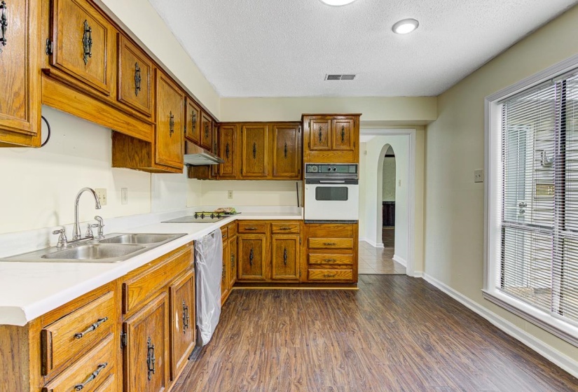 Kitchen featuring extensive wood cabinetry, white countertops, a double basin stainless steel sink, built-in wall oven, and wood-finish flooring