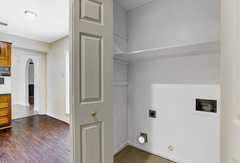 Utility closet featuring a bi-fold door, recessed shelving, and hookups for laundry appliances